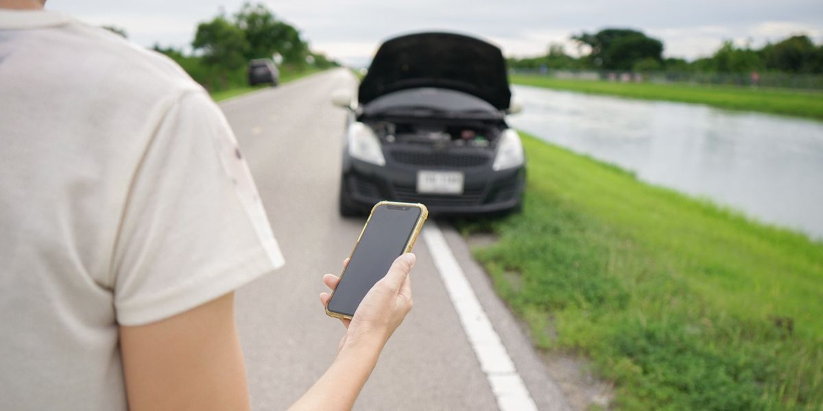 Woman's hand using smartphone to call auto mechanic with broken car on the roadside. A woman is holding a mobile phone and calling for help with a broken down car on the road.