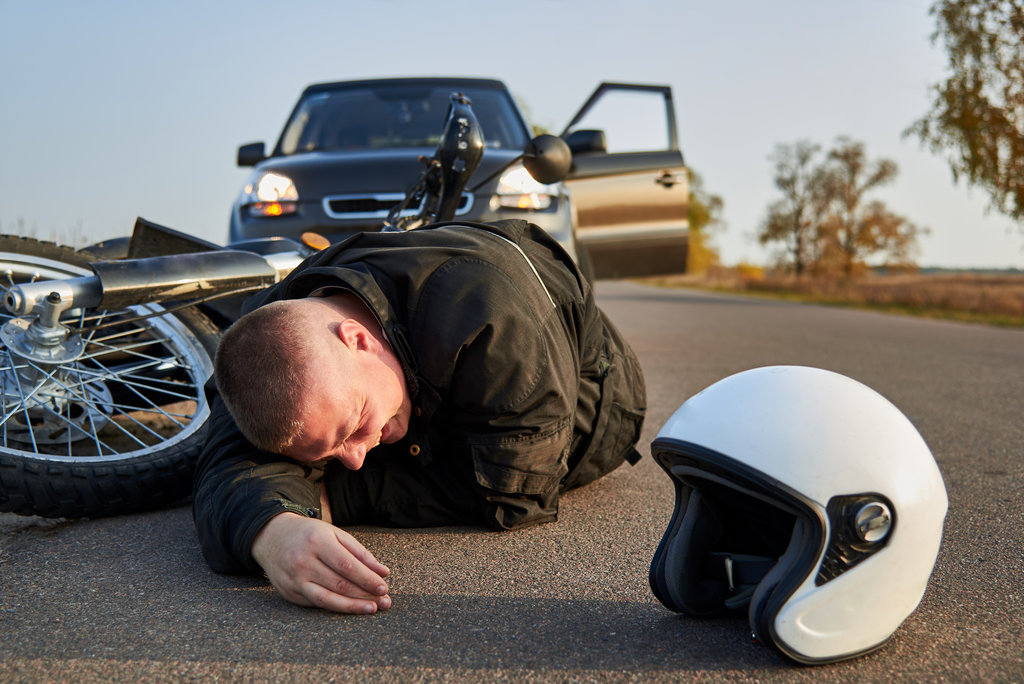 A motorcyclist lies on the asphalt near a motorcycle and car, the theme of road accidents.