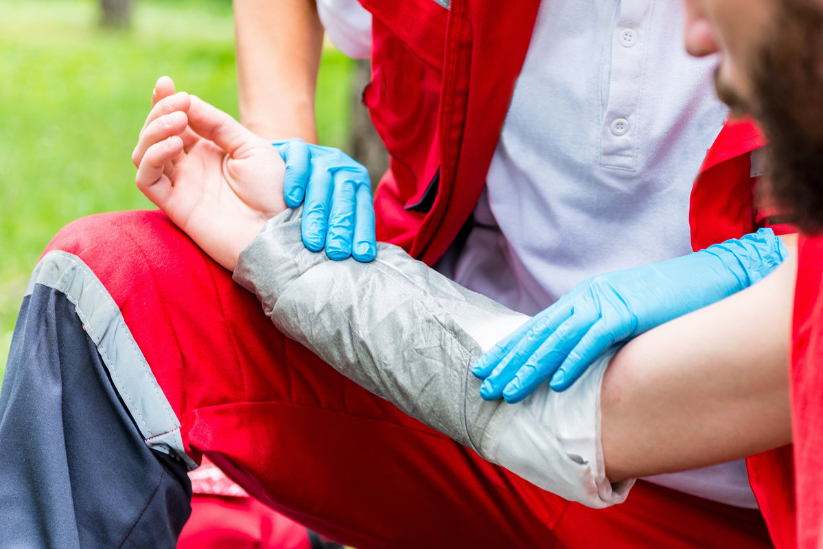 Medical worker treating burns on male's hand. First aid treatment outdoors. First aid practice
