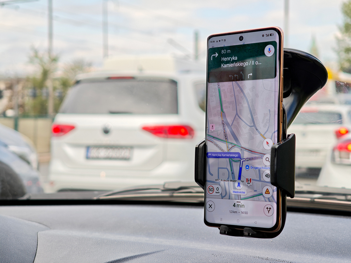 Smartphone with Google Maps navigation app open, smartphone in a windshield mount inside vehicle, route guidance speed alerts city traffic, turn-by-turn directions on phone screen commuting, nobody